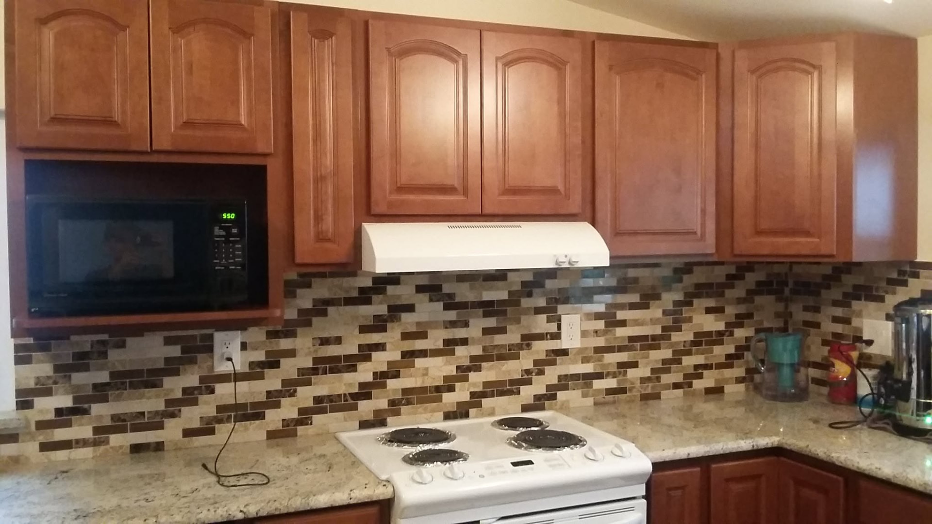 Completed mosaic tile backsplash installation above a kitchen range